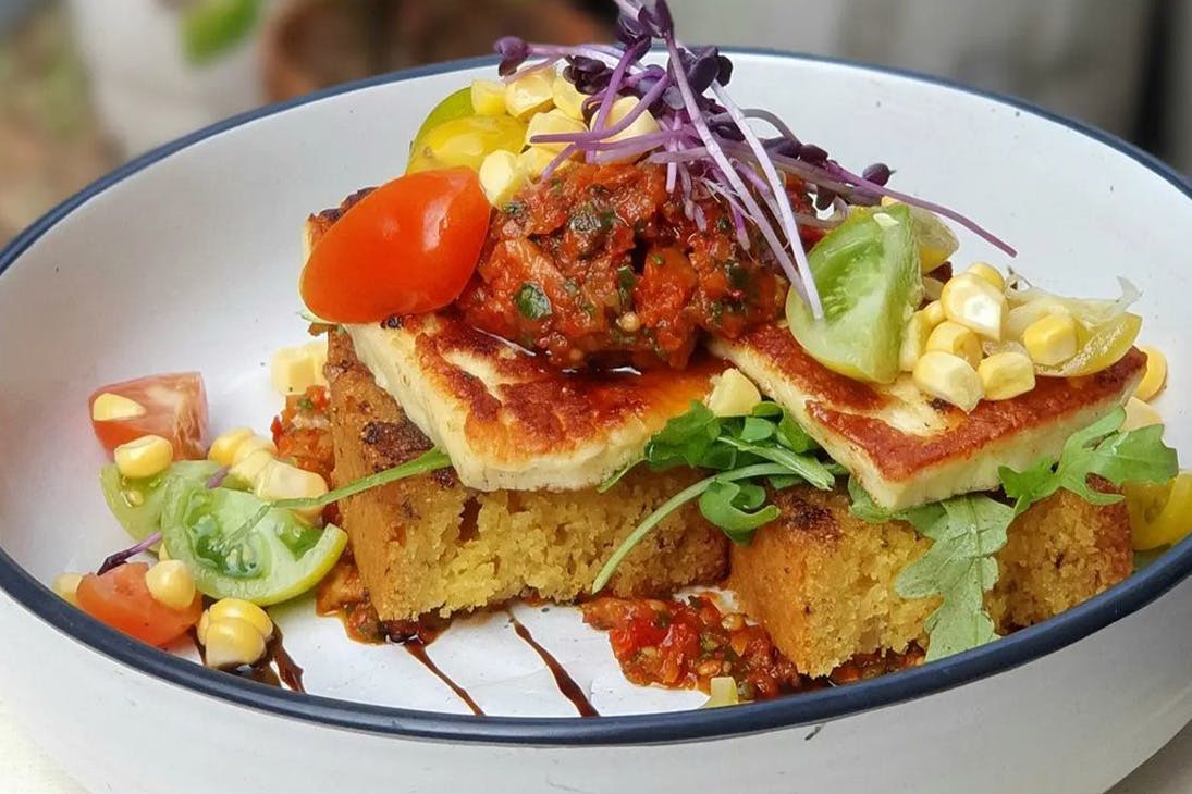 Thick, soft toast with halloumi, relish, tomato, corn and sprouts stacked on.